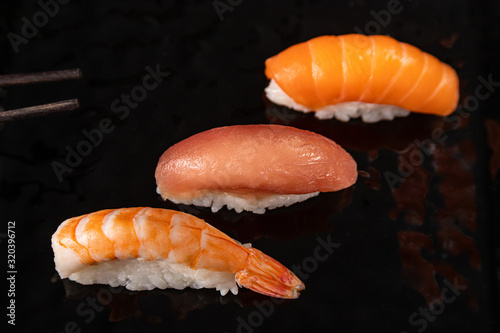 Nigiri sushi set with shrimp, salmon and tuna on black glossy plate, selected focus