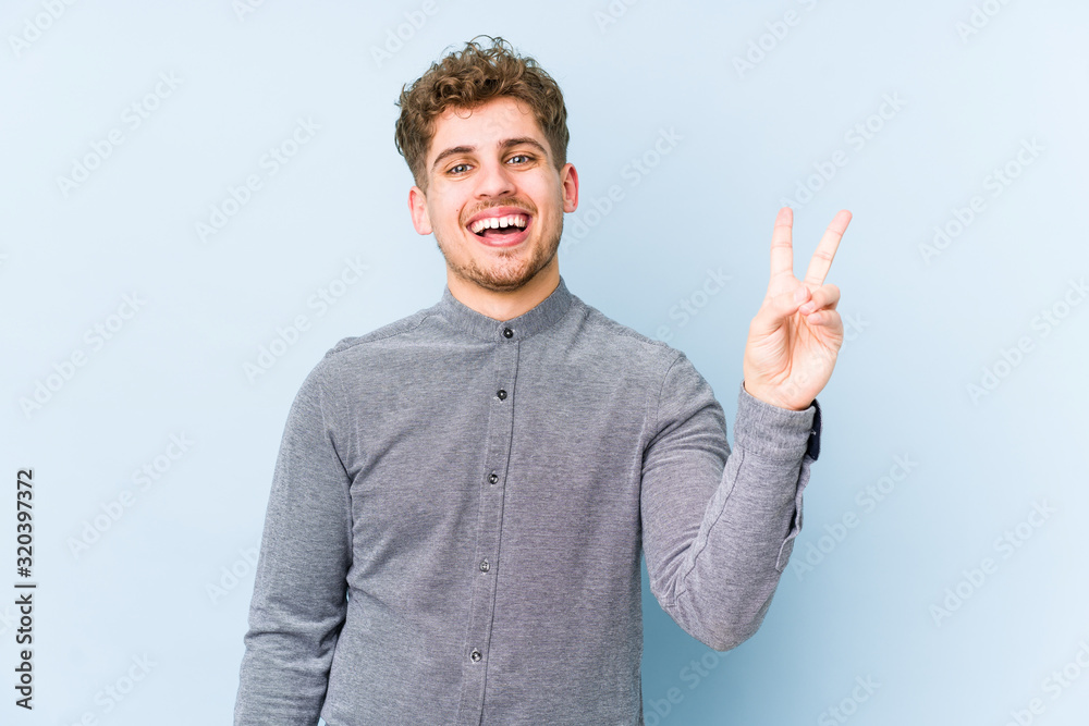 Young blond curly hair caucasian man isolated joyful and carefree showing a peace symbol with fingers. Young blond curly hair caucasian man isolated joyful and carefree showing a peace symbol with fingers.
