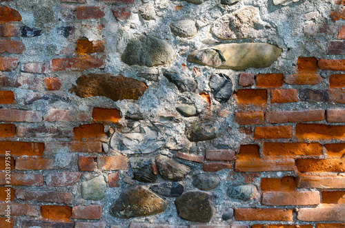 the sun's rays illuminate part of the old brick wall restored with the help of stone cobblestones