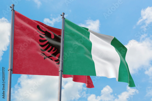Nigeria and Albania flags waving in the wind against white cloudy blue sky together. Diplomacy concept, international relations.