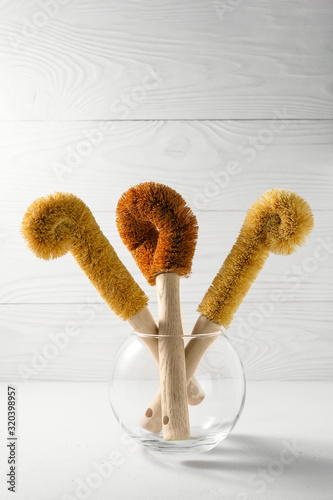 Three coconut scrapers for washing dishes in a glass vase. Biodegradable kitchen accessories and zero waste concept. Image contains copy space.