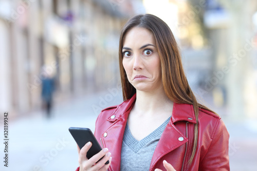 Perplexed woman using phone looks at camera photo