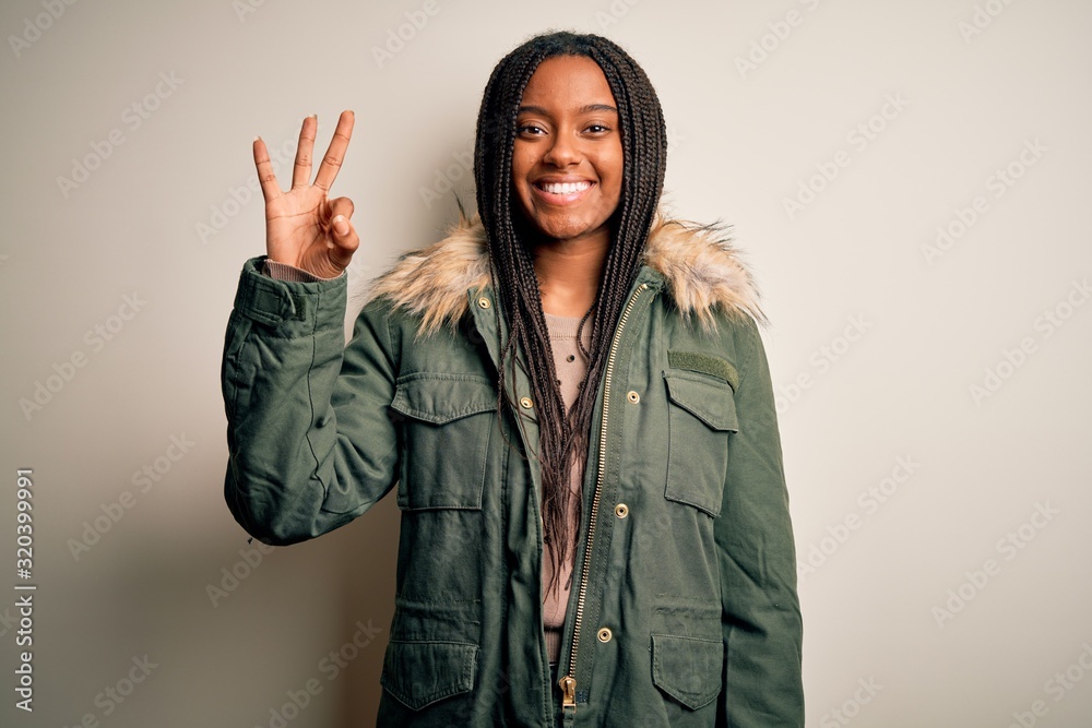Young african american woman wearing winter parka coat over isolated background showing and pointing up with fingers number three while smiling confident and happy. Young african american woman wearing winter parka coat over isolated background showing and pointing up with fingers number three while smiling confident and happy.