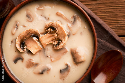 Close-up top view of a bowl of mushroom soup with a wooden spoon on a wooden table