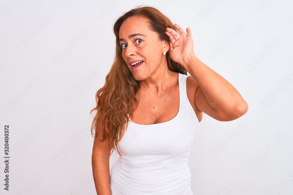 Middle age mature woman standing over white isolated background smiling with hand over ear listening an hearing to rumor or gossip. Deafness concept. Middle age mature woman standing over white isolated background smiling with hand over ear listening an hearing to rumor or gossip. Deafness concept.