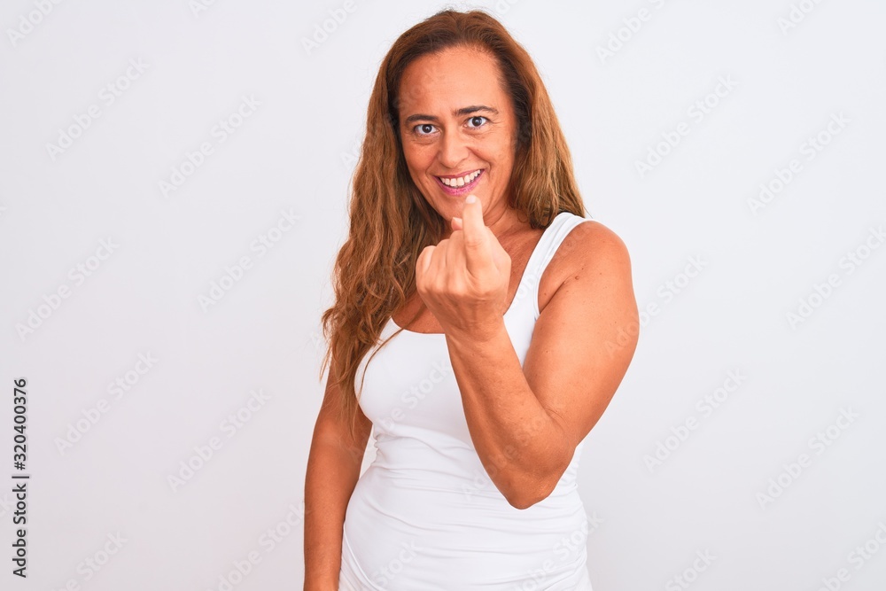 Middle age mature woman standing over white isolated background Beckoning come here gesture with hand inviting welcoming happy and smiling