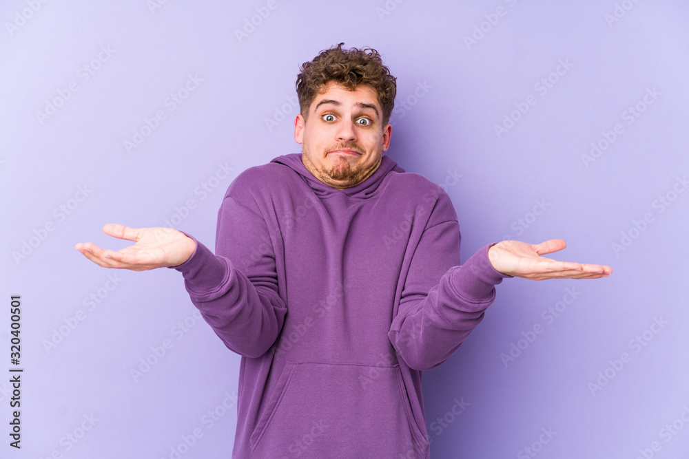 Fototapeta premium Young blond curly hair caucasian man isolated doubting and shrugging shoulders in questioning gesture.