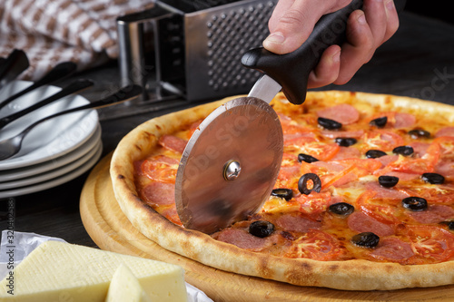 Pizza on the board and pizza knife in the hands of the waiter. Man cut the closed italian pizza with a knife. Delicious Large meat pizza with bacon, sausage, salami, pepperoni and olives.