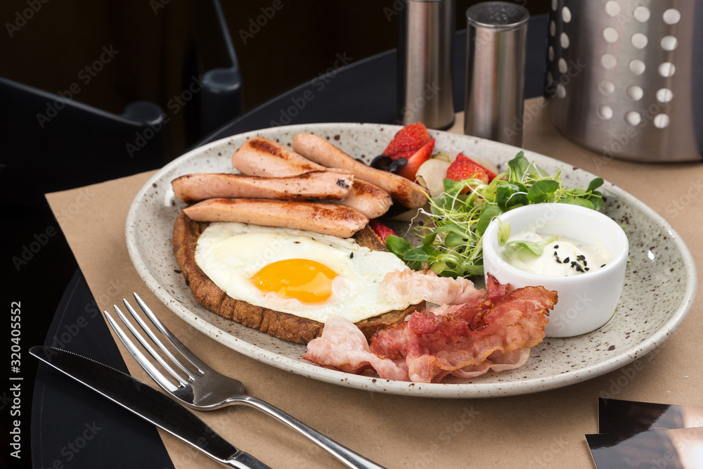 Homemade delicious american breakfast with sunny side up fried egg, toast, sausage, fruits, vegetable, strawberry jam, croissant