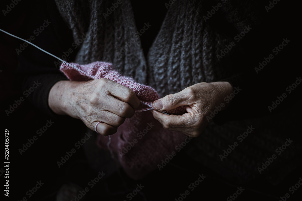 The old woman sits at home and knits garments. Close up.