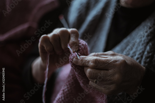 The old woman sits at home and knits garments. Close up.