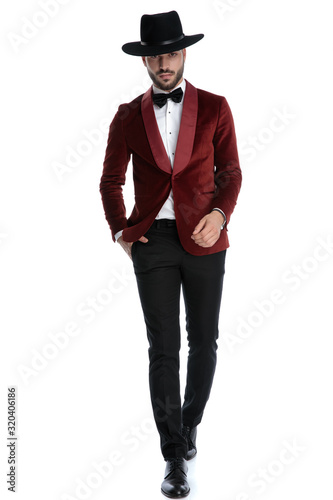 elegant fashion man in red velvet tuxedo wearing hat and walking