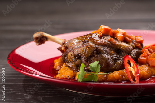 Grilled duck leg with vegetables. Roasted duck with Vegetables served on a red plate. Space for text, closeup.
