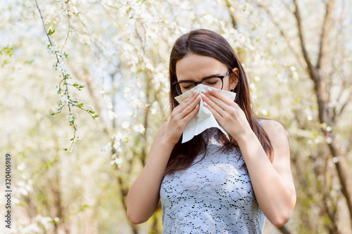 Student girl in glasses holds handkerchief near her face while sneezing or blowing her nose in spring. Symbol of spring illness