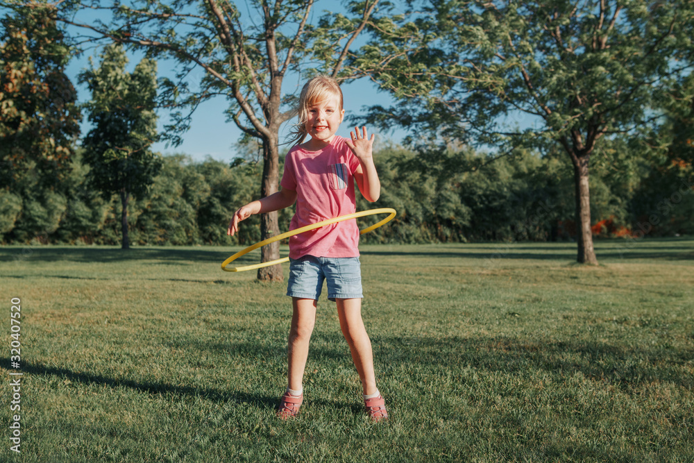 Cute smiling Caucasian preschool girl playing with hoola hoop in park outside. Kids sport activity. Lifestyle happy childhood. Summer seasonal outdoors game fun for kids children. Cute smiling Caucasian preschool girl playing with hoola hoop in park outside. Kids sport activity. Lifestyle happy childhood. Summer seasonal outdoors game fun for kids children.