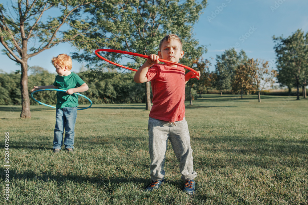 Fototapeta premium Two cute Caucasian preschool boys playing with hoola hoop in park outside. Kids sport activity. Lifestyle happy childhood. Summer seasonal outdoors game fun for kids children.
