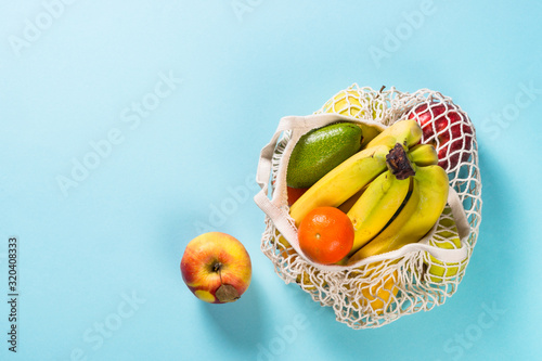 Mesh bag with fruits on color background.