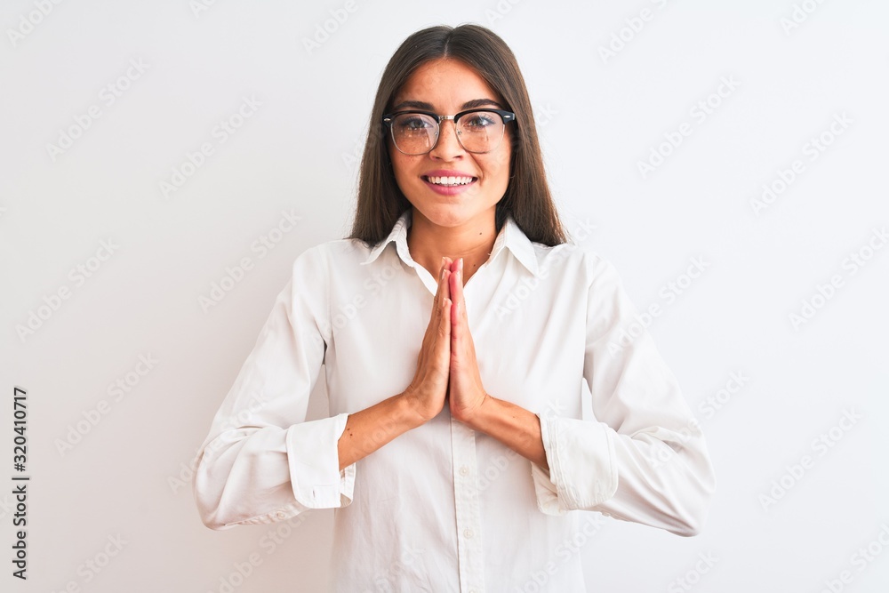Young beautiful businesswoman wearing glasses standing over isolated white background praying with hands together asking for forgiveness smiling confident. Young beautiful businesswoman wearing glasses standing over isolated white background praying with hands together asking for forgiveness smiling confident.