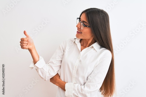 Young beautiful businesswoman wearing glasses standing over isolated white background Looking proud, smiling doing thumbs up gesture to the side