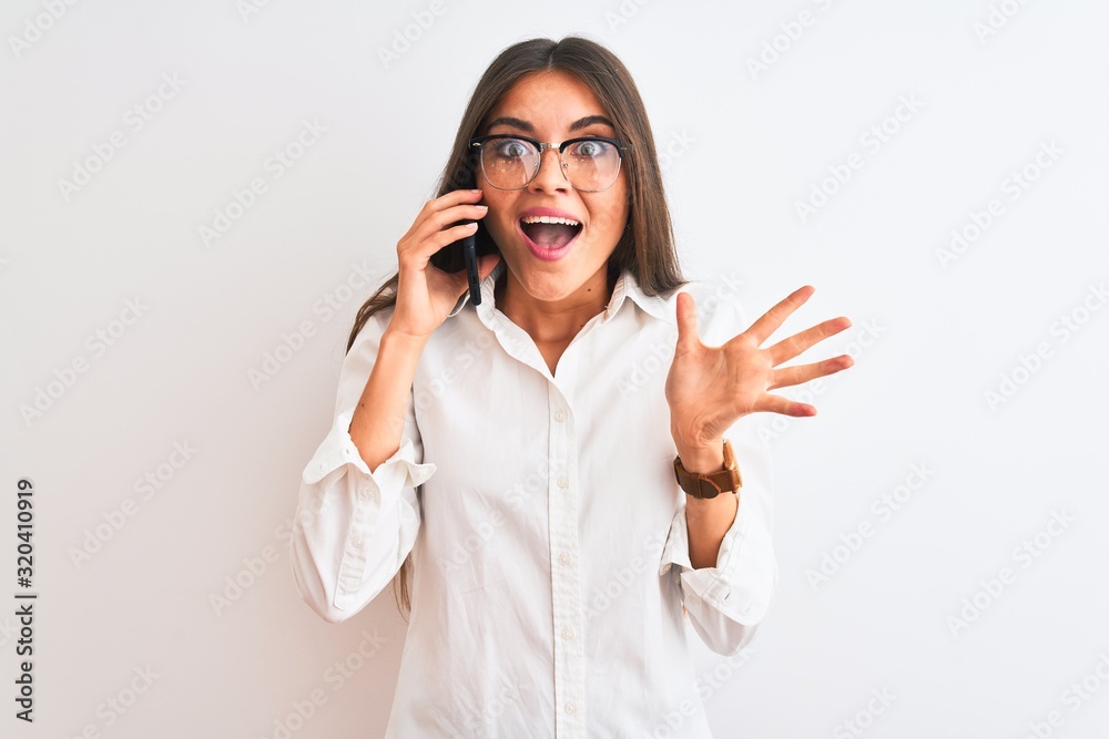Young businesswoman wearing glasses talking on smartphone over isolated white background very happy and excited, winner expression celebrating victory screaming with big smile and raised hands Young businesswoman wearing glasses talking on smartphone over isolated white background very happy and excited, winner expression celebrating victory screaming with big smile and raised hands