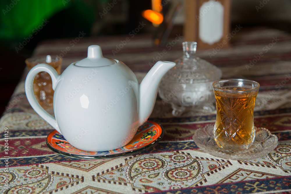 Fototapeta premium Tea in Azerbaijani traditional armudu pear-shaped glass . Azerbaijan black tea .white sugar cubes . White kettle and sugar bowl . Ceramic white teapot . Azerbaijani aromatic tea in armudu cup .