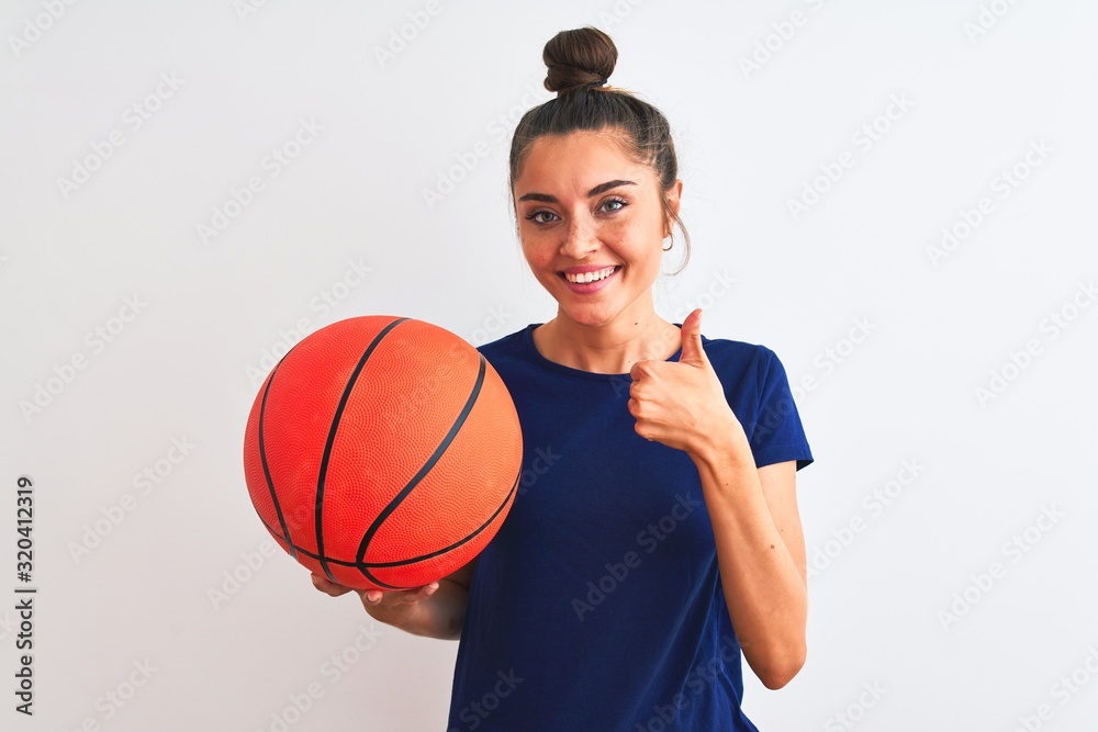 Young beautiful sportswoman holding basketball ball over isolated white background happy with big smile doing ok sign, thumb up with fingers, excellent sign