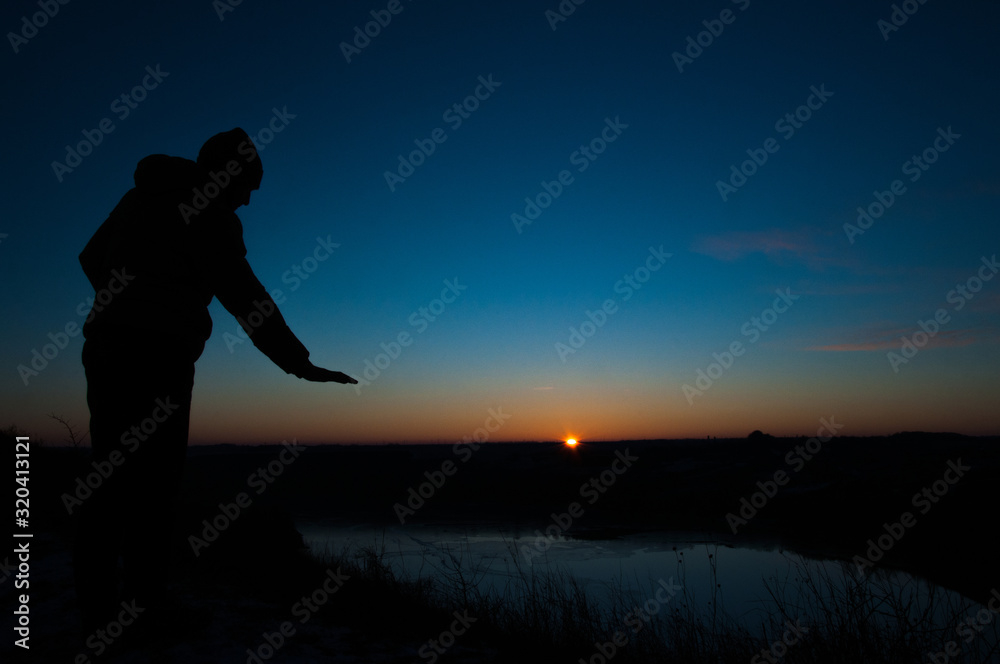 Silhouetted men on a background of blue sky and sunset. With arms raised. Prayer to God. Glorification.