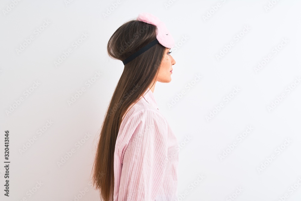 Young beautiful woman wearing sleep mask and pajama over isolated white background looking to side, relax profile pose with natural face and confident smile.