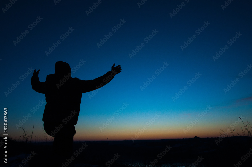 Silhouetted men on a background of blue sky and sunset. With arms raised. Prayer to God. Glorification.