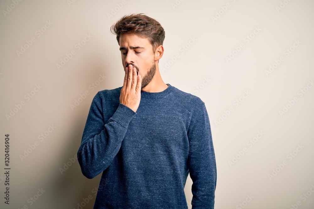 Young handsome man with beard wearing casual sweater standing over white background bored yawning tired covering mouth with hand. Restless and sleepiness. Young handsome man with beard wearing casual sweater standing over white background bored yawning tired covering mouth with hand. Restless and sleepiness.