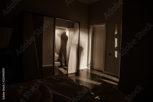Fotografie A creepy bedroom scenery, Silhouette of scary person standing reflected in mirror with mist and toned light