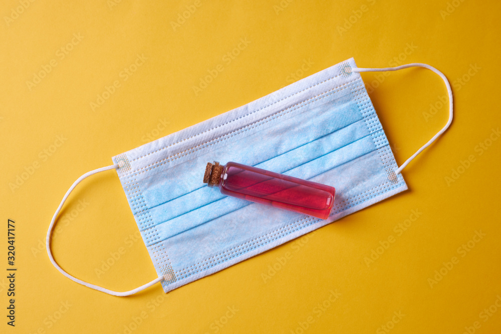 vial with red liquid over blue face mask on yellow background. virus and infection protection concept. flat lay. vial with red liquid over blue face mask on yellow background. virus and infection protection concept. flat lay.