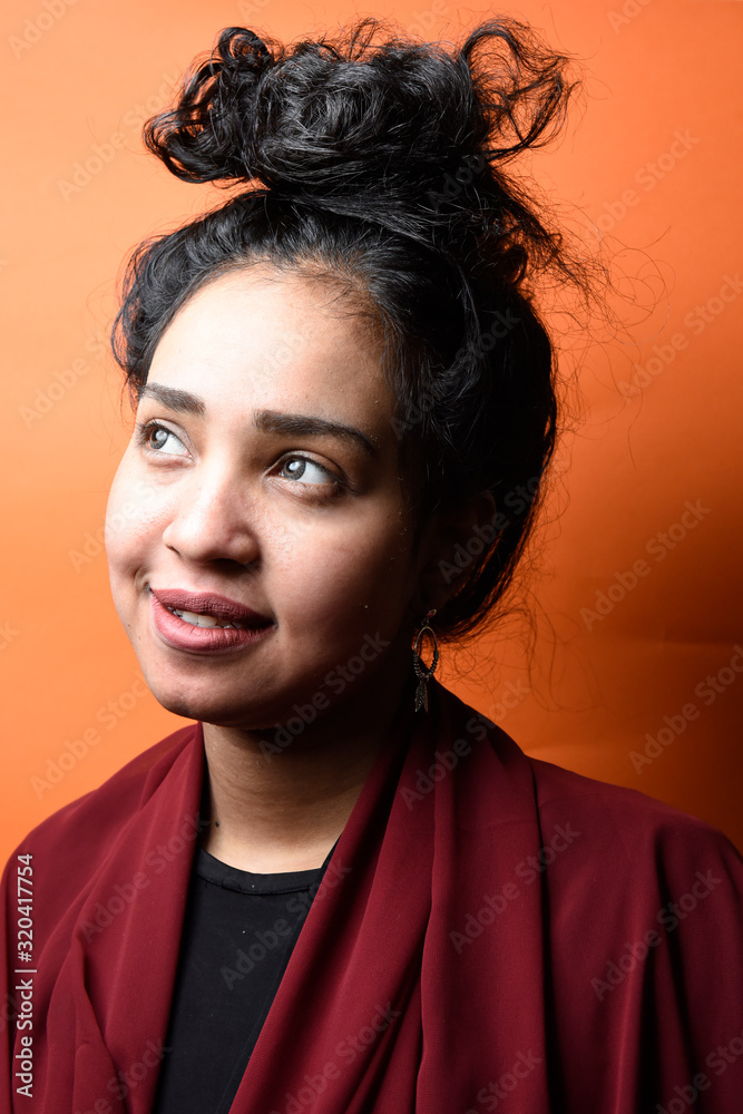 Studio shot of young beautiful Egyptian teenage girl with black hair against orange background Studio shot of young beautiful Egyptian teenage girl with black hair against orange background
