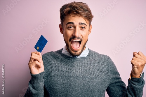 Vászonkép Young customer man with beard holding credit card for payment over pink backgrou