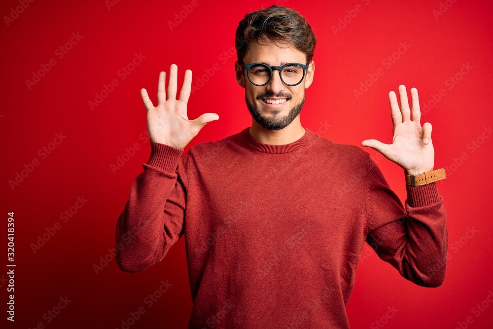Young handsome man with beard wearing glasses and sweater standing over red background showing and pointing up with fingers number nine while smiling confident and happy. Young handsome man with beard wearing glasses and sweater standing over red background showing and pointing up with fingers number nine while smiling confident and happy.