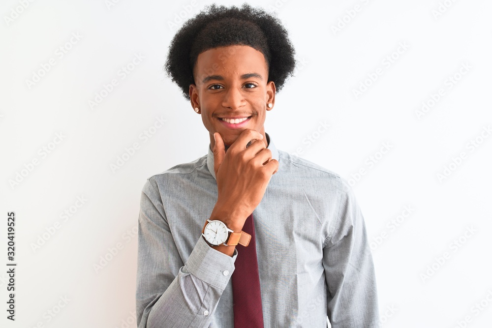 Young african american businessman wearing tie standing over isolated white background looking confident at the camera with smile with crossed arms and hand raised on chin. Thinking positive. Young african american businessman wearing tie standing over isolated white background looking confident at the camera with smile with crossed arms and hand raised on chin. Thinking positive.