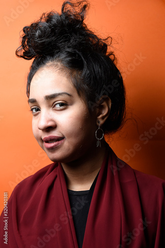 Studio shot of young beautiful Egyptian teenage girl with black hair against orange background