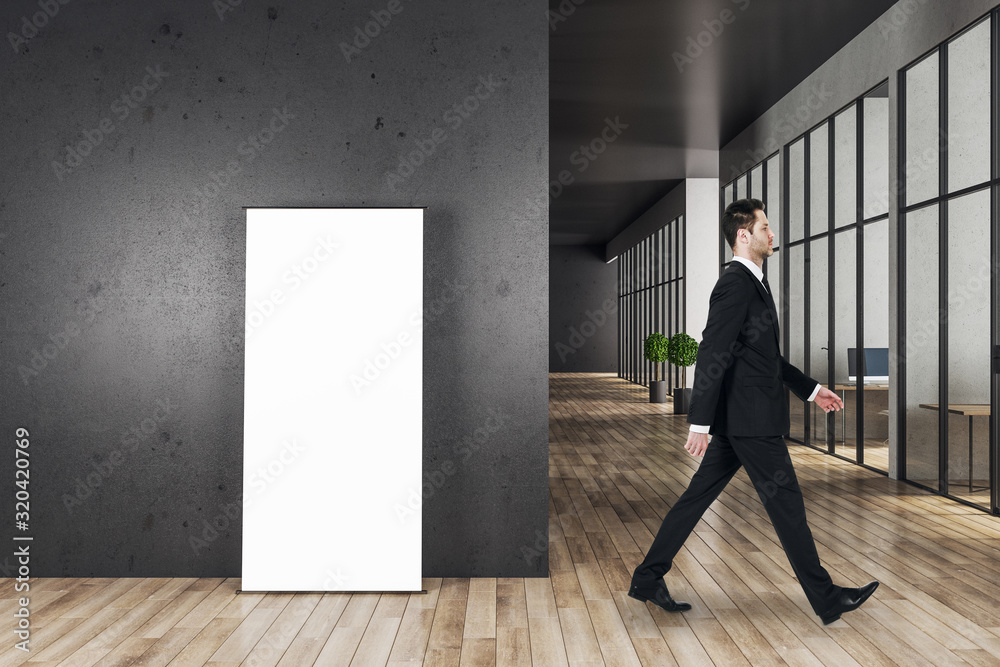 Businessman walking in office interior with blank banner Businessman walking in office interior with blank banner