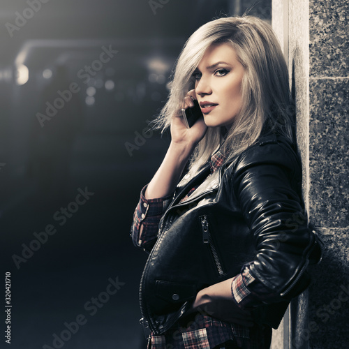 Young fashion blonde woman in leather jacket talking on cell phone