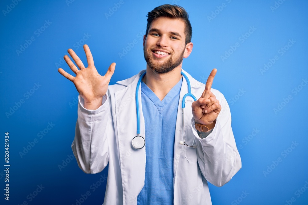Young blond doctor man with beard and blue eyes wearing white coat and stethoscope showing and pointing up with fingers number six while smiling confident and happy.