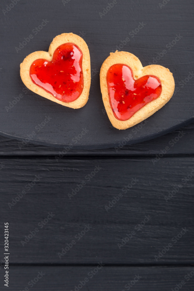 Obraz premium Heart shaped cookies decorated for Valentine's Day. Free space for text. Two heart shaped cookies with jam on a black wooden table. Like postcard 