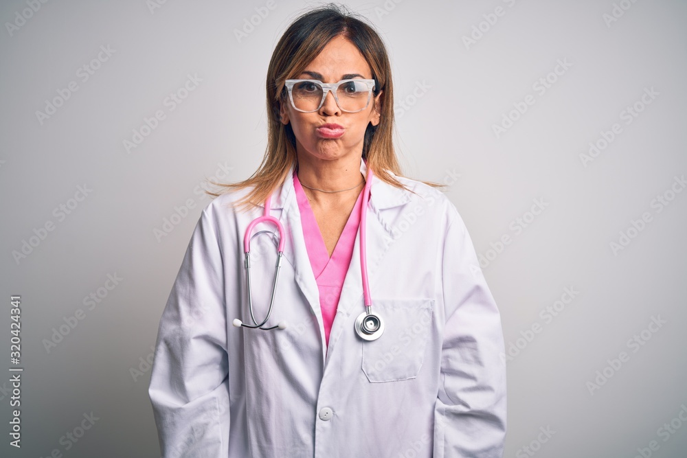 Middle age beautiful doctor woman wearing pink stethoscope over isolated white background puffing cheeks with funny face. Mouth inflated with air, crazy expression. Middle age beautiful doctor woman wearing pink stethoscope over isolated white background puffing cheeks with funny face. Mouth inflated with air, crazy expression.