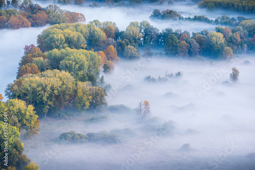 Abstract with Airuno on Adda river in Italy at sunrise with myst fog trees foliage in autumn fall season photo