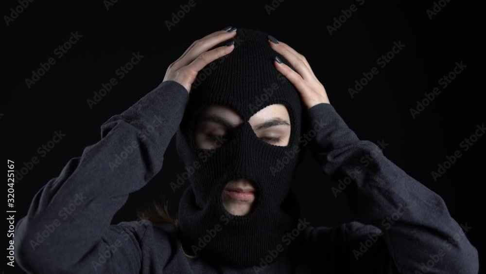 A young woman is putting on a balaclava mask. Bandit on a black ...