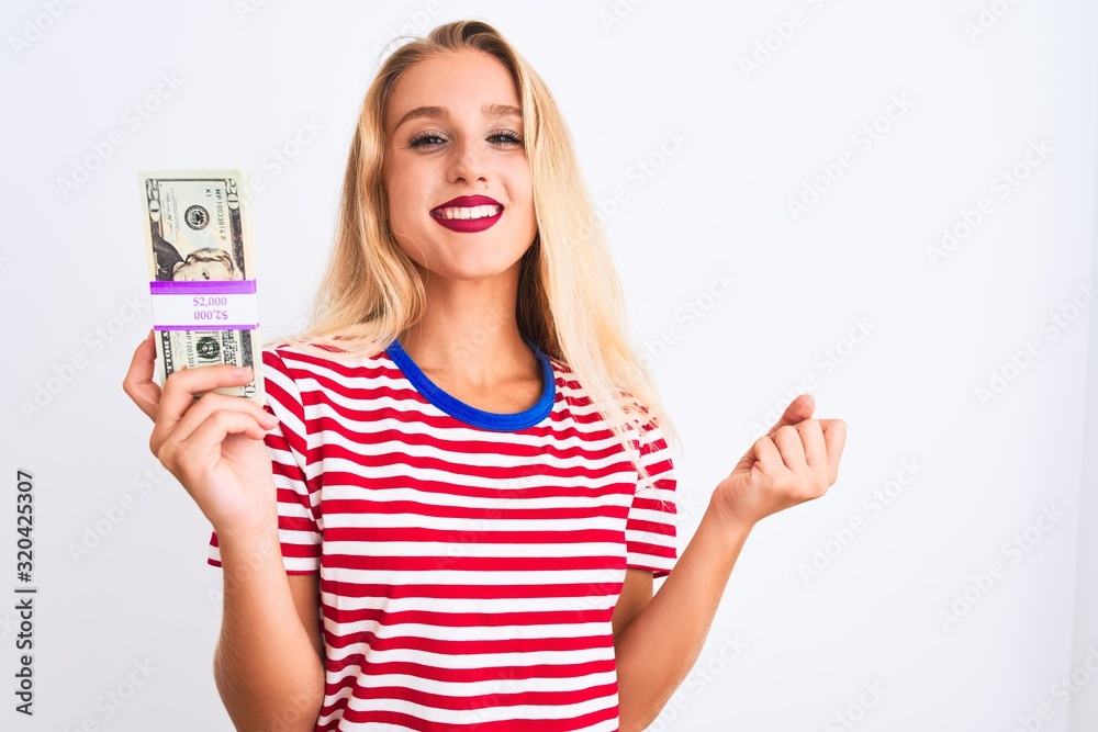 Beautiful woman wearing red striped t-shirt holding dollars over isolated white background screaming proud and celebrating victory and success very excited, cheering emotion Beautiful woman wearing red striped t-shirt holding dollars over isolated white background screaming proud and celebrating victory and success very excited, cheering emotion