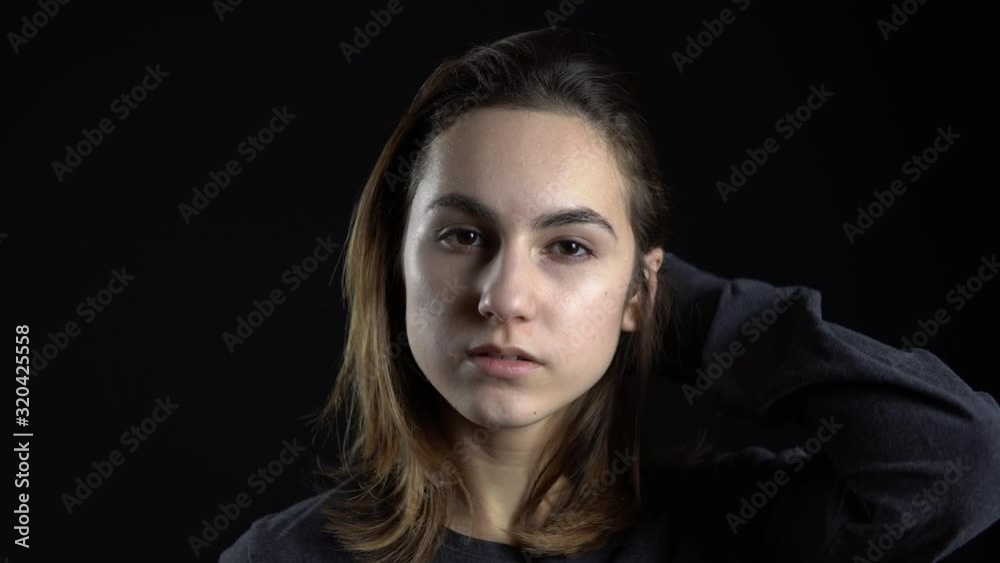 A young woman takes off the mask of a balaclava. Bandit on a black background close-up. A young woman takes off the mask of a balaclava. Bandit on a black background close-up.