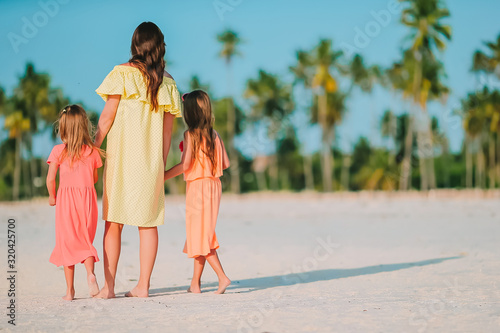 Adorable little girls and young mother on white beach