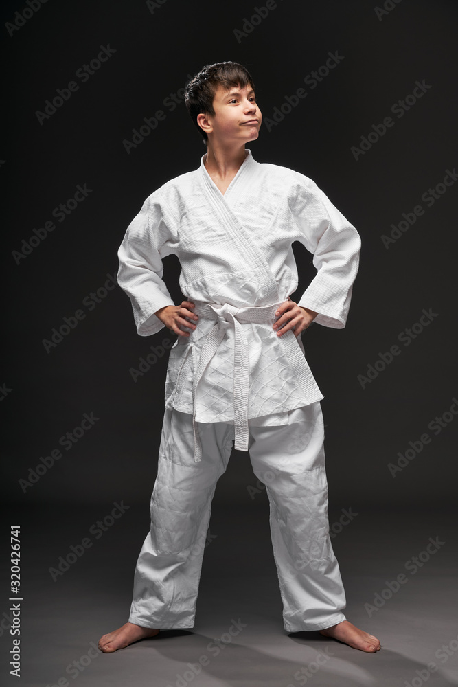 a teenager dressed in martial arts clothing poses on a dark gray background, a sports concept a teenager dressed in martial arts clothing poses on a dark gray background, a sports concept