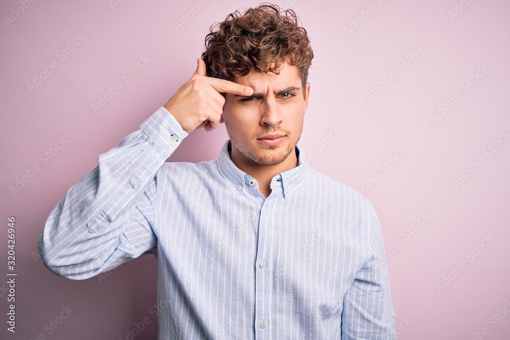 Young blond handsome man with curly hair wearing striped shirt over white background pointing unhappy to pimple on forehead, ugly infection of blackhead. Acne and skin problem Young blond handsome man with curly hair wearing striped shirt over white background pointing unhappy to pimple on forehead, ugly infection of blackhead. Acne and skin problem