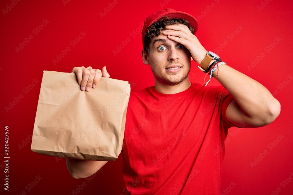 Young blond delivery man with curly hair wearing cap holding paper bag with food stressed with hand on head, shocked with shame and surprise face, angry and frustrated. Fear and upset for mistake. Young blond delivery man with curly hair wearing cap holding paper bag with food stressed with hand on head, shocked with shame and surprise face, angry and frustrated. Fear and upset for mistake.
